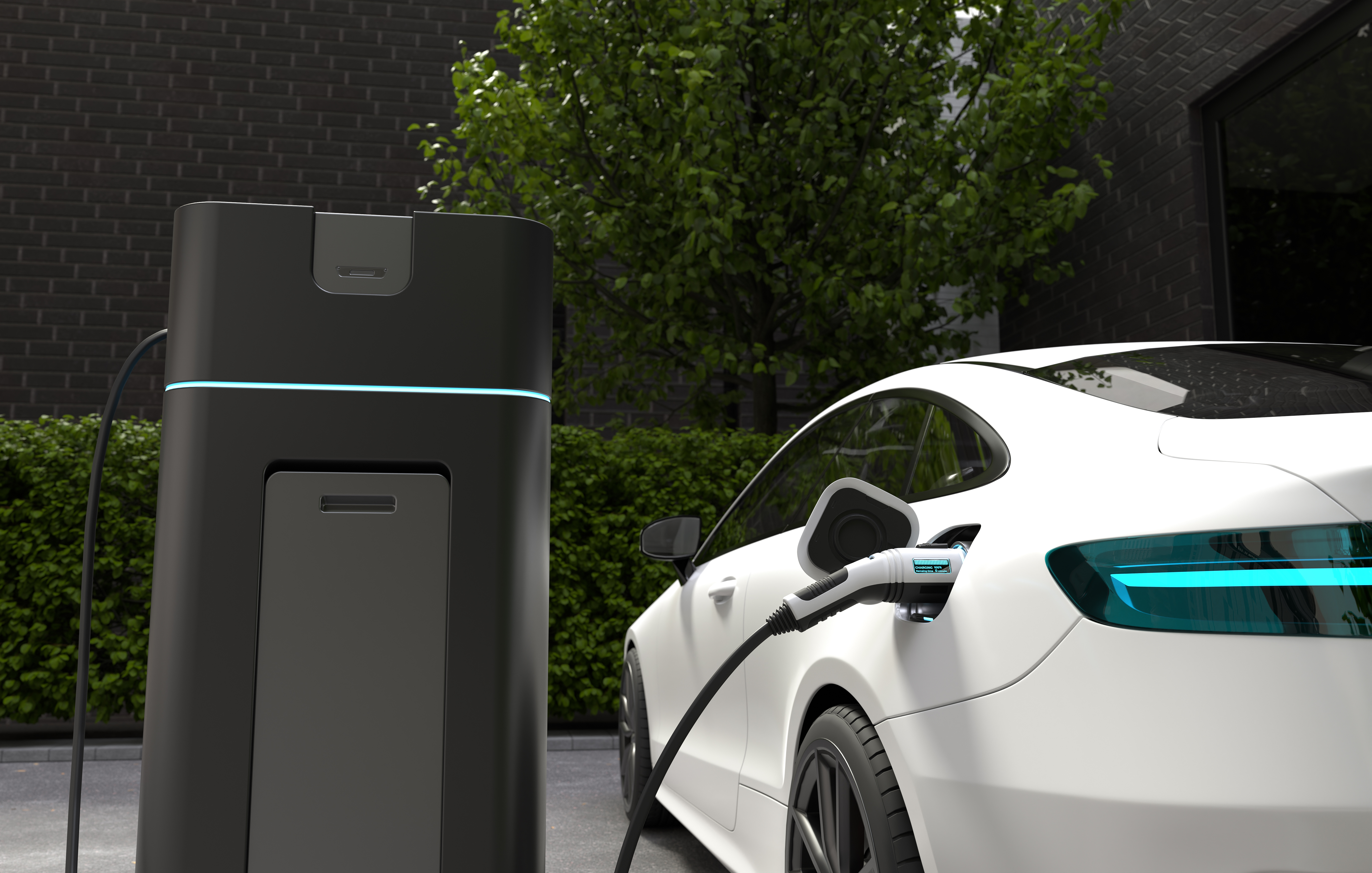 Modern white electric car plugged into a sleek black EV charger home installation station outside a dark brick residence.