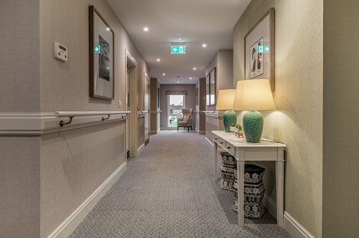 Well-lit care home corridor with illuminated emergency exit signs and professional electrical installations, demonstrating the electrical infrastructure requiring regular EICR testing for resident safety and regulatory compliance.